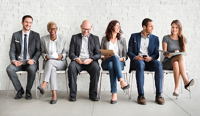Men and women in business casual clothing sitting in a row waiting to be interviewed for a job